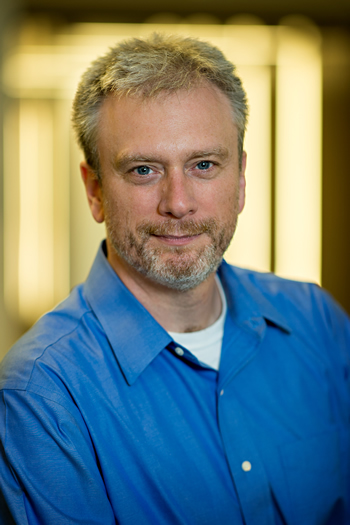 Portrait of man with gray hair and blue shirt on a yellow background