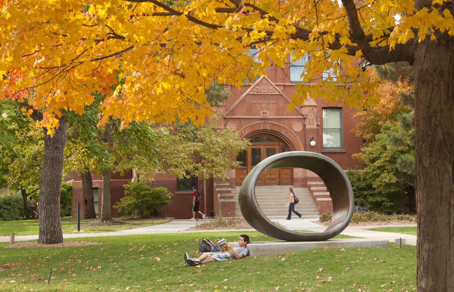 Student reads outdoors on campus surrounded by fall foliage